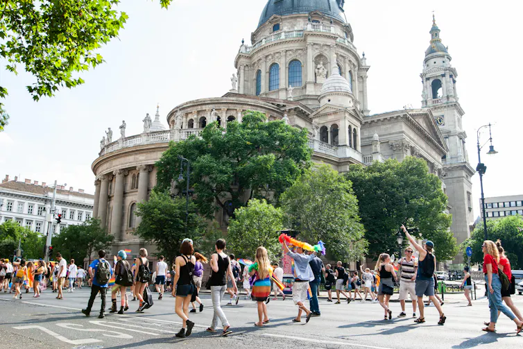 Men and women walk through city street, some with rainbow flags and clothing.
