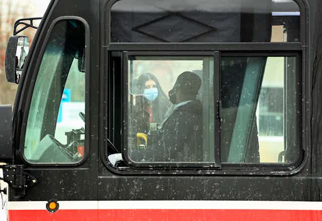 A bus driver and a passenger seen through a bus window