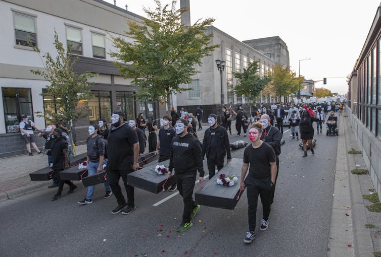 A crowd of people march, some carrying mock coffins