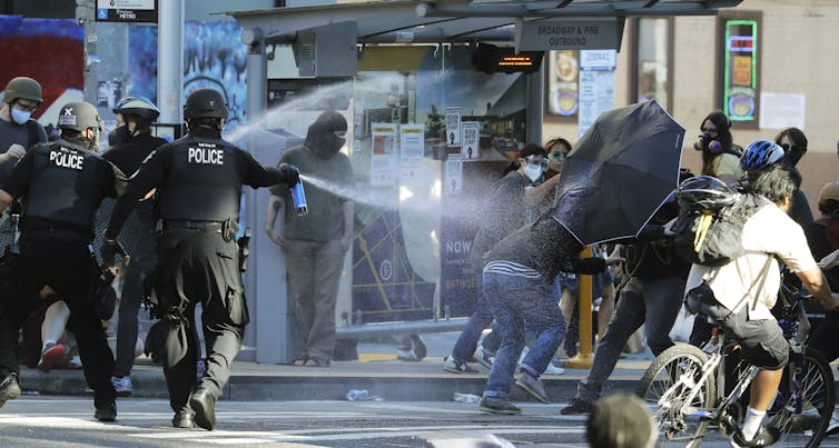 Police in protective gear spray chemical agents at demonstrators