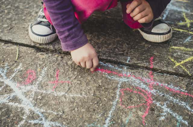 Un enfant dessine sur le sol avec une craie.