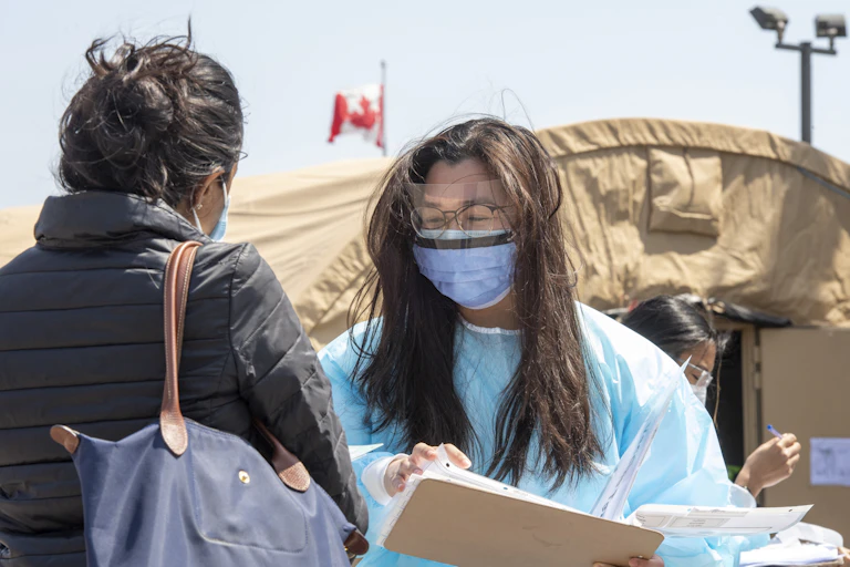 A health-care worker in personal protective equipment talks to a woman wearing a mask at an outdoor vaccine clinic.