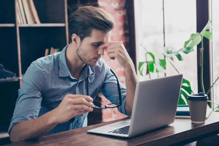 A young man using a laptop appears stressed.