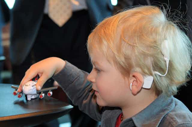 young boy with a cochlear ear implant plays with a toy plane