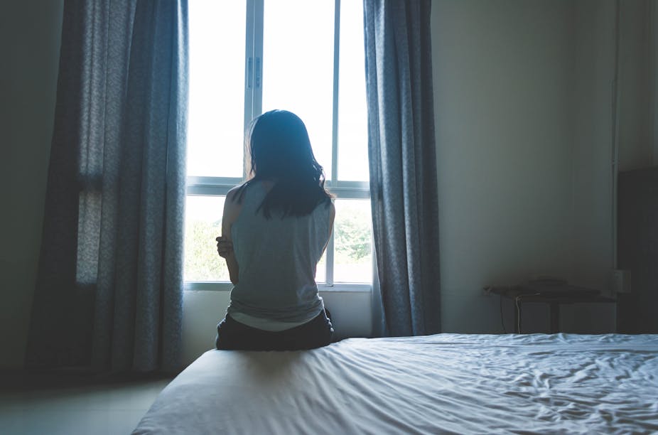 A woman sits on a bed while looking out the window.
