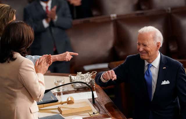 A smiling President Biden gestures to Vice President Harris and Speaker Nancy Pelosi after giving a speech to Congress