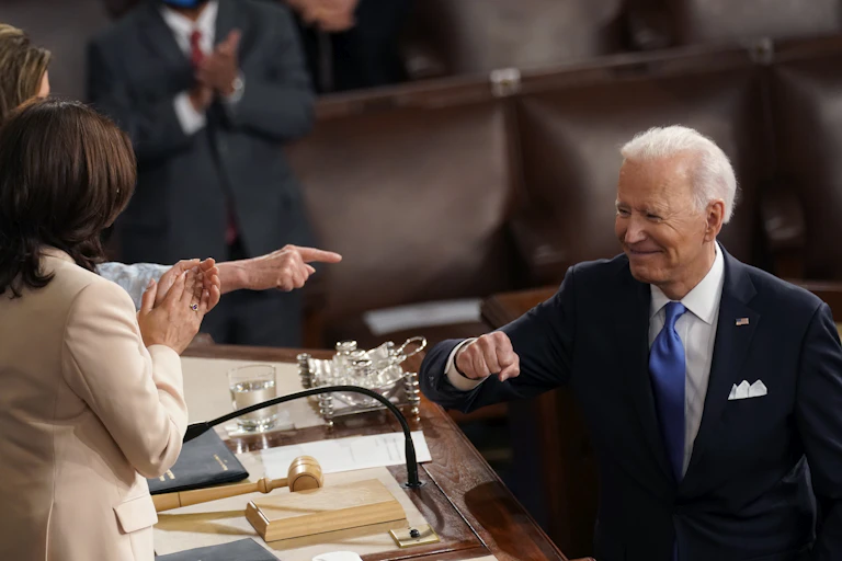 A smiling President Biden gestures to Vice President Harris and Speaker Nancy Pelosi after giving a speech to Congress
