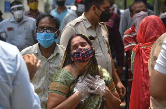 A woman with mask and gloves clutches her heart after hearing of the death of a family member, New Delhi, India, April 29 2021