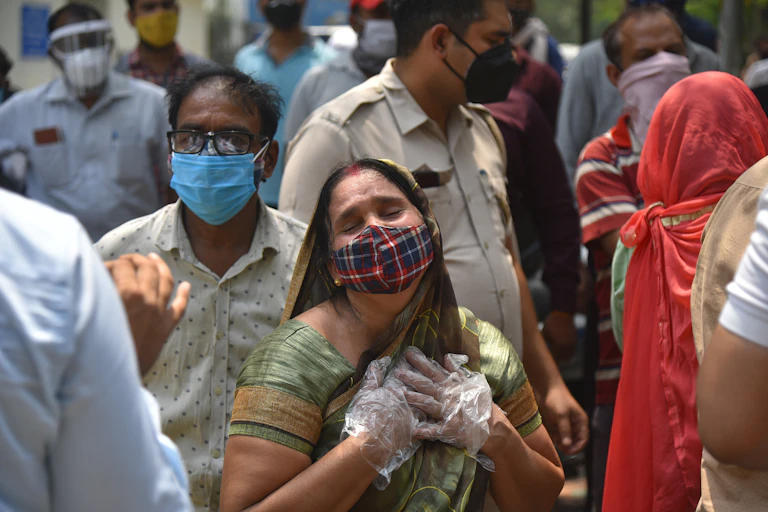 A woman with mask and gloves clutches her heart after hearing of the death of a family member, New Delhi, India, April 29 2021