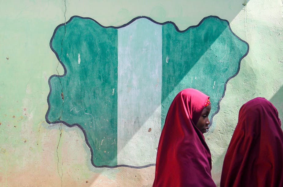 Two girls in front of a drawing of a map of Nigeria on a wall.
