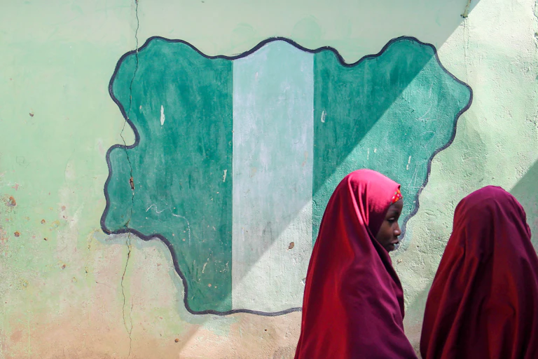 Two girls in front of a drawing of a map of Nigeria on a wall.