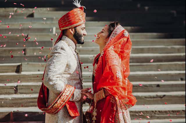 Indian couple on their wedding day, standing by steps surrounded by floating petals