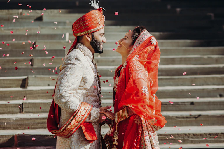 Indian couple on their wedding day, standing by steps surrounded by floating petals
