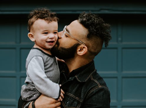 A father holds a baby boy in front of a blue door