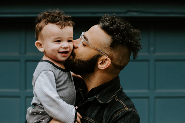 A father holds a baby boy in front of a blue door