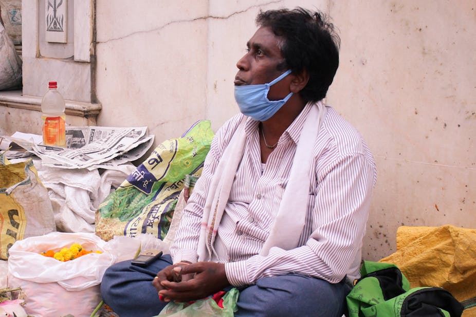 Indian man with a face mask sellling goods outside a temple