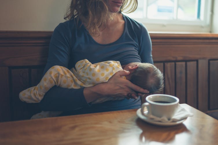 A woman breastfeeds her baby while having a coffee in a cafe