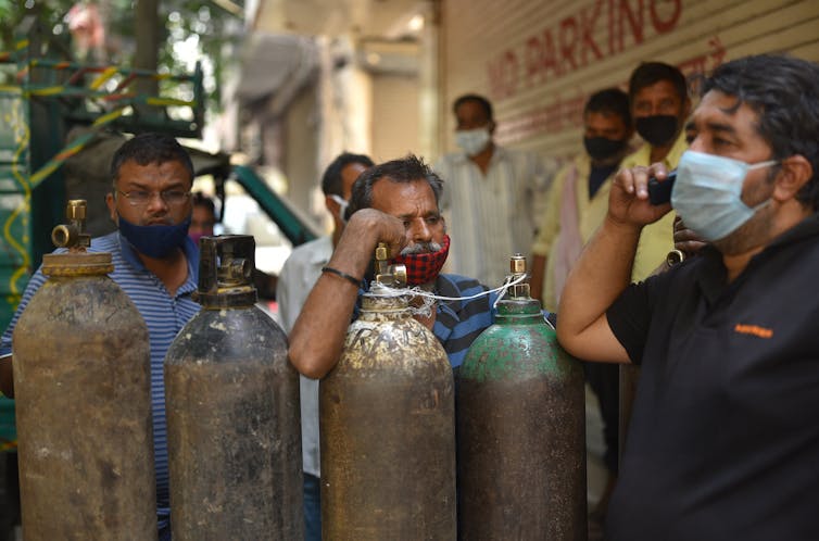 Men wearing COVID masks queue to buy oxygen, while a man talks on a mobile phone.