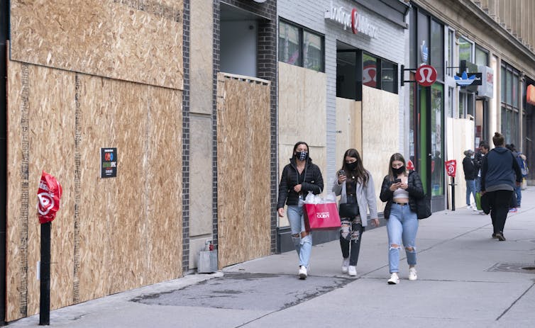 People walk past boarded-up storefront