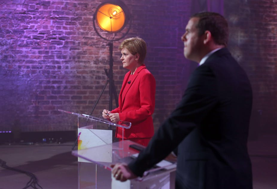 Nicola Sturgeon and Douglas Ross stand behind podiums during televised election debate. 