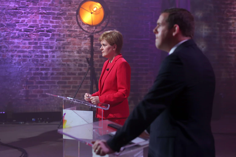 Nicola Sturgeon and Douglas Ross stand behind podiums during televised election debate.