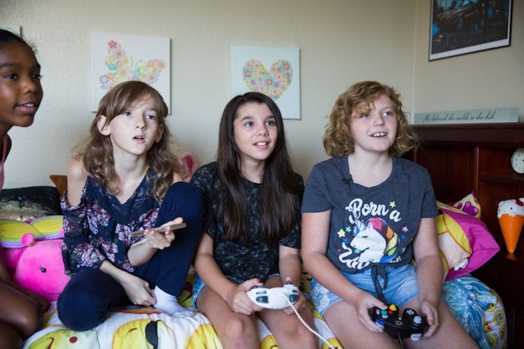 Four kids sit on a bed playing video games.