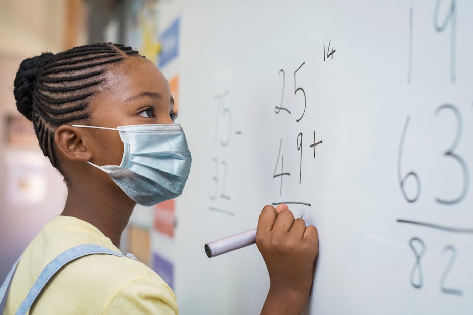 Young Black girl standing at a white board, working on a math problem.