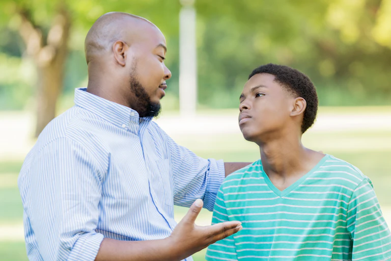 A father talks to his upset son outside.