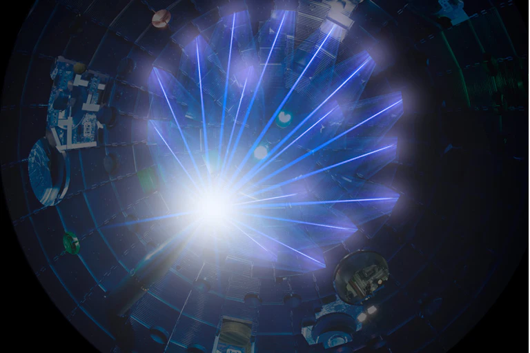 A series of laser beams converge at the tip of a spike projecting into the middle of a cylindrical chamber