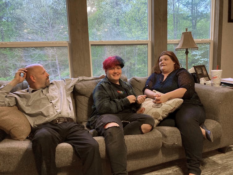 Andrew Bostad, a transgender youth, sitting on the sofa at home with his mother and stepfather.