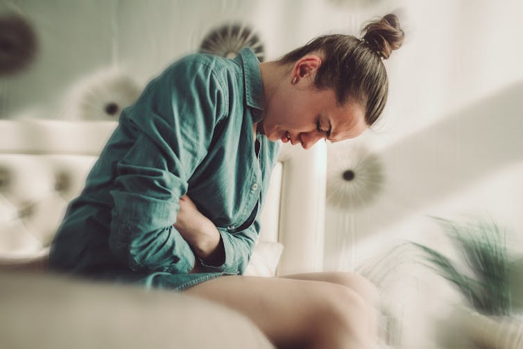 A young woman hunched over, apparently having stomach pains.