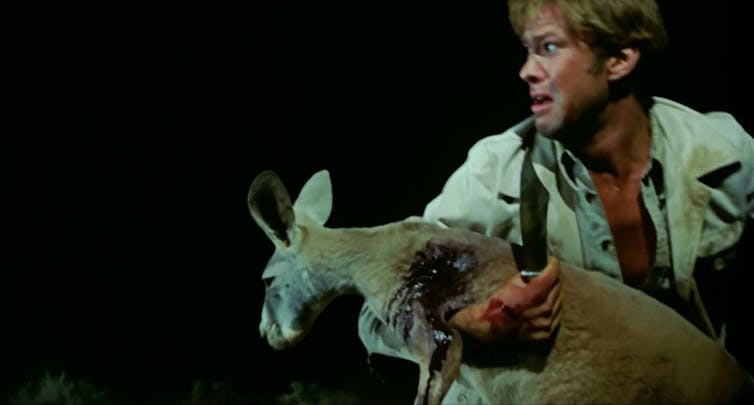 Production image: a man holds a bleeding kangaroo.