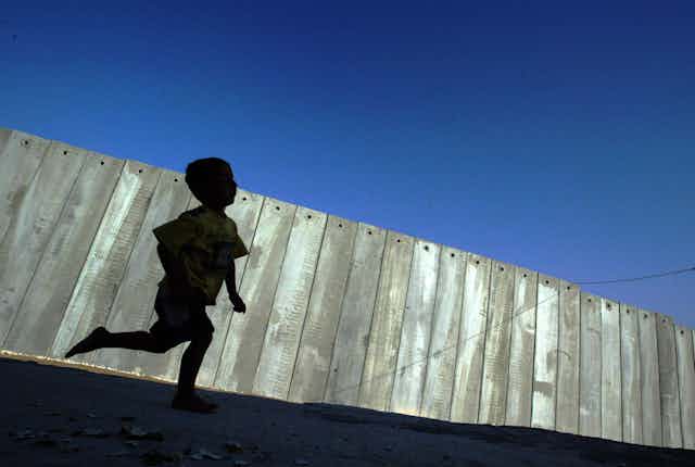 A young Palestinian boy playing in the shadow of the 'security fence' between Israel and the Occupied Palestinian Territory 