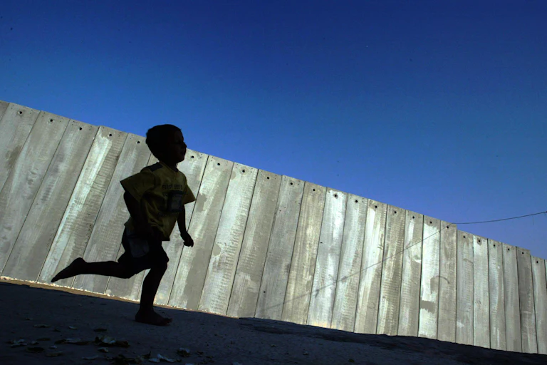 A young Palestinian boy playing in the shadow of the 'security fence' between Israel and the Occupied Palestinian Territory
