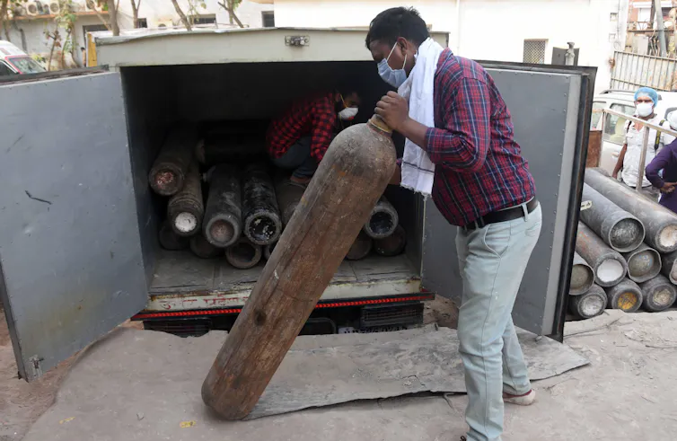 A man holding an oxygen cylinder, in front of a truck full of them.