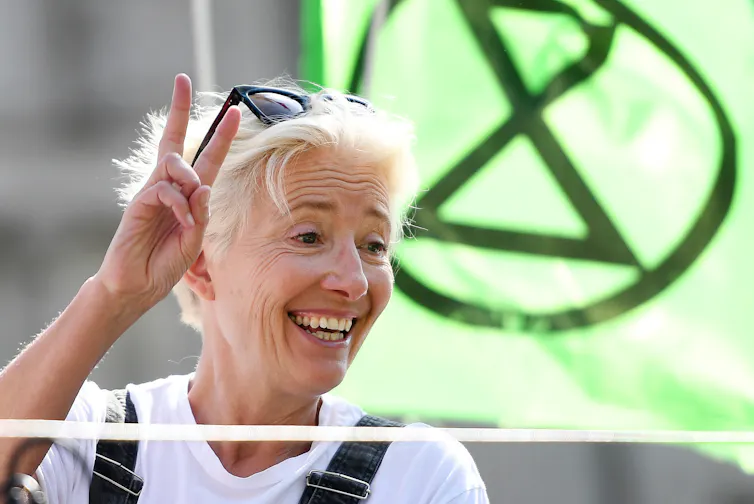 Woman gives peace sign in front of green banner