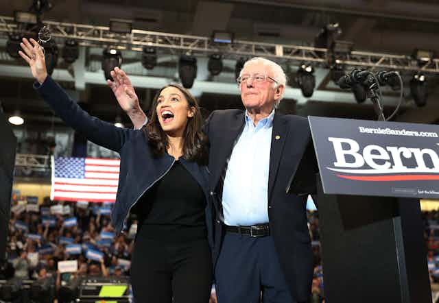 AOC and Sanders wave to the crowd at a rally