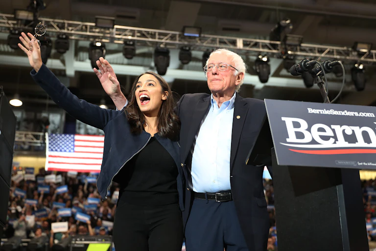 AOC and Sanders wave to the crowd at a rally