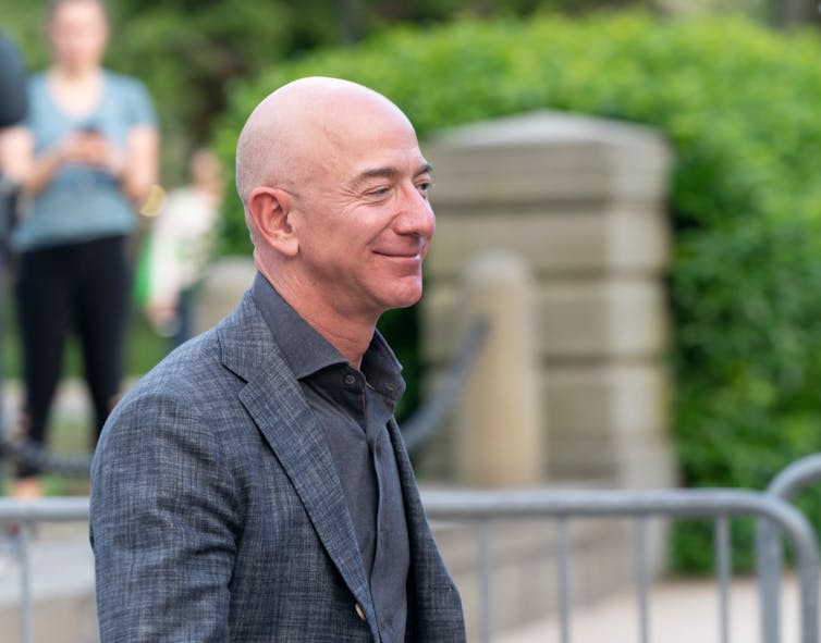 Jeff Bezos stood outside, smiling and wearing a grey suit