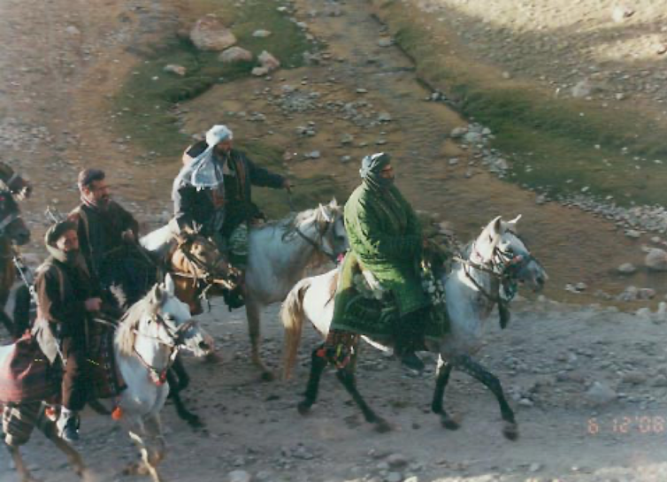 Armed men ride horses through rocky ground
