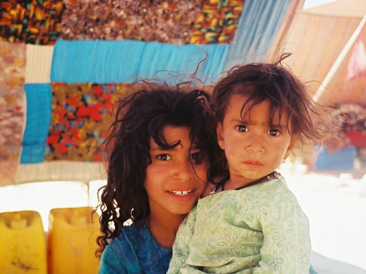 A young girl and her brother sit under a fabric tent