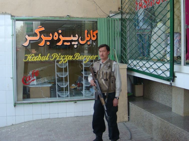 A man with a rifle stands in front of a restaurant window