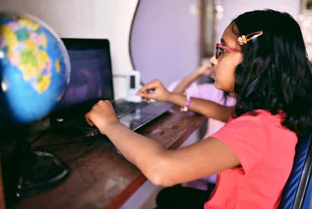 A young girl sits at her computer desk.