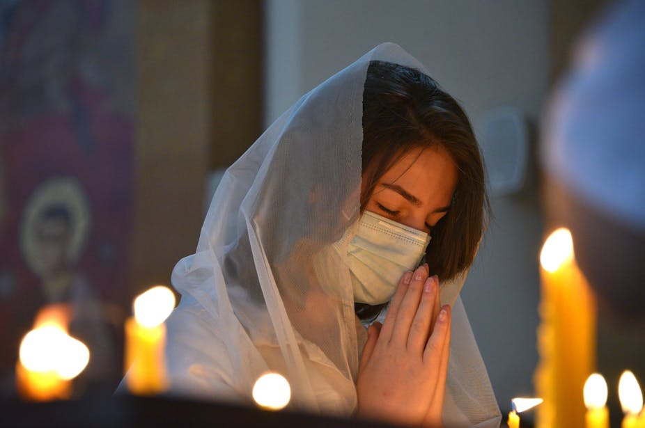 A woman, wearing a face mask, prays in a church.