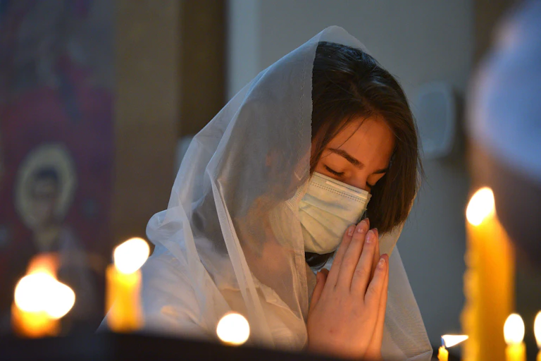 A woman, wearing a face mask, prays in a church.