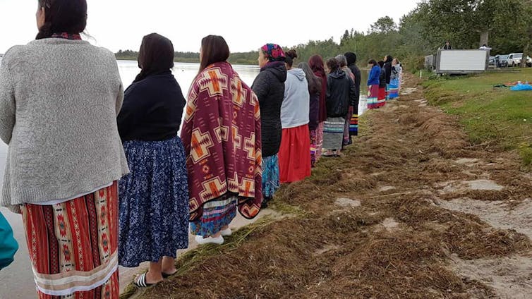 Women stand in a row looking out at a lake.