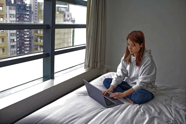 Asian student sitting on bed as she uses laptop