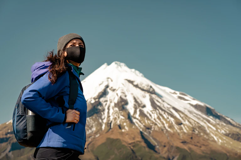 Una mujer con mochila y mascarilla en la montaña.