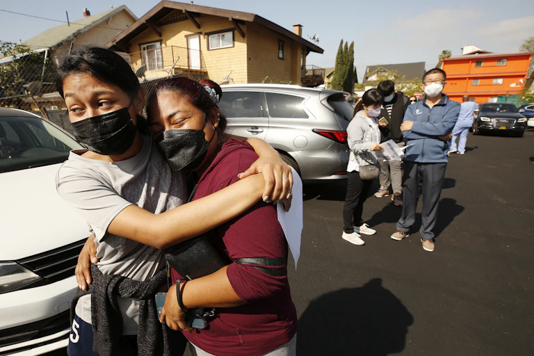 A mother and daughter hug as they way in line to receive COVID-19 vaccination
