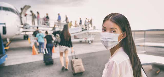 A woman in a face mask looks back as a line of people board a small plane ahead of her